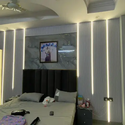Bedroom with a fluted panel wall lit by vertical LED strips behind a marble-look headboard backdrop, and a tufted black upholstered bed.