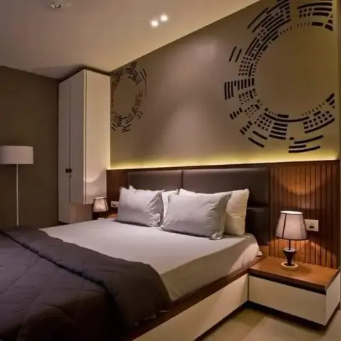 Bedroom with a fluted wood headboard panel lit by a concealed strip, a dark upholstered headboard between wall-hung white bedside drawers