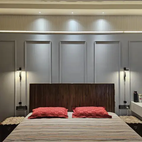 Bedroom with a fluted wood slat headboard set against a panel-moulded grey feature wall lit by twin wall sconces.