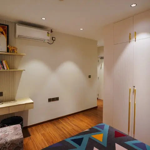 Bedroom with a full-height fluted wardrobe with brass handles, a built-in study desk and open shelf, and warm wood-plank flooring.