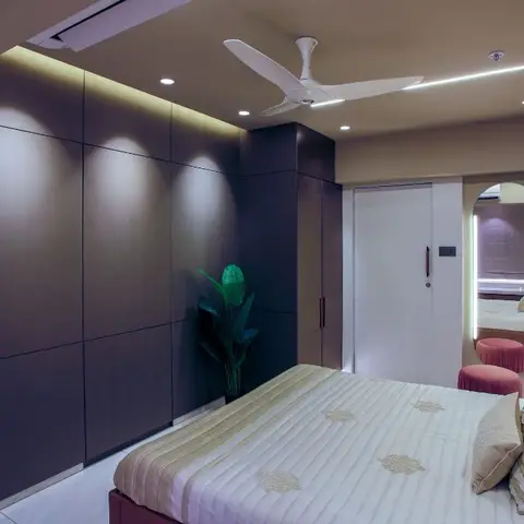 Bedroom with a full-height fluted dark wardrobe wall, cove-lit ceiling, and an arched backlit mirror beside the entry door.