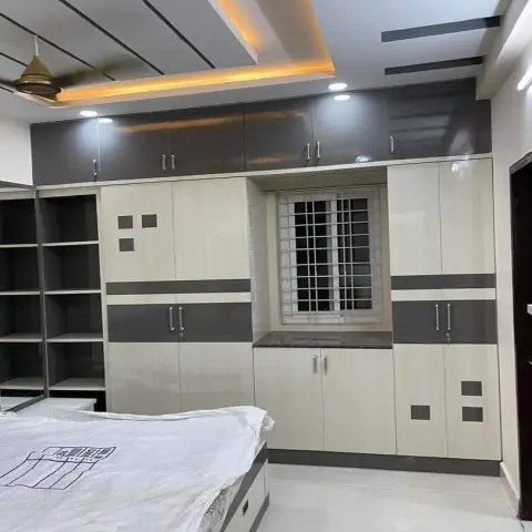 Bedroom with a full-height grey-and-white laminate wardrobe wall, a mirrored dresser at the foot of the bed, and a cove-lit false ceiling.