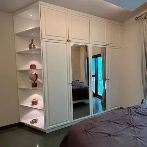Bedroom with a full-height white panel-shutter wardrobe including mirrored center doors and a lit open corner display shelf