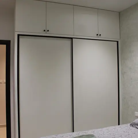 Bedroom with a full-height white sliding-door wardrobe with black trim and matching loft cabinets, beside a textured grey accent wall.