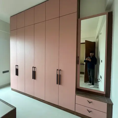 Bedroom with a full-length pastel pink laminate wardrobe run and a matching dresser unit with a full-height mirror and two drawers.
