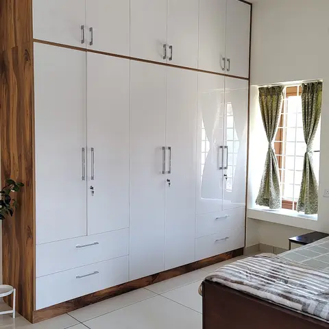 Bedroom with a full-wall high-gloss white wardrobe framed in natural wood grain, sage-green patterned curtains