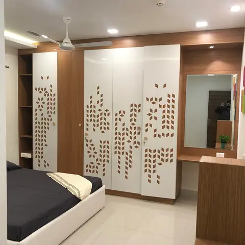 Bedroom with a full-wall wardrobe featuring laser-cut chevron wood-inlay shutters and an attached dressing mirror unit.