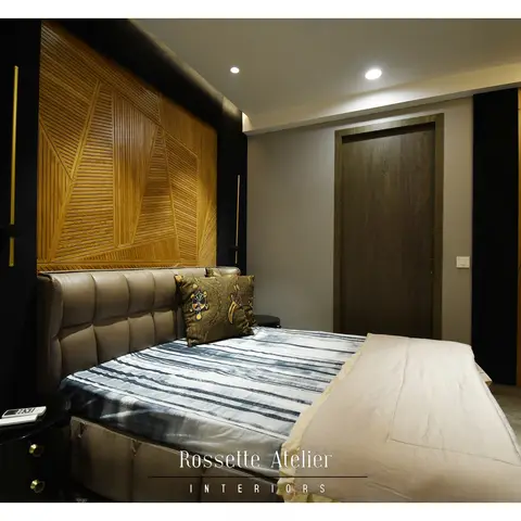 Bedroom with a geometric wood fin panel headboard wall, a grey tufted leather bed, black accent walls, and a guitar displayed on the wood-paneled wardrobe.