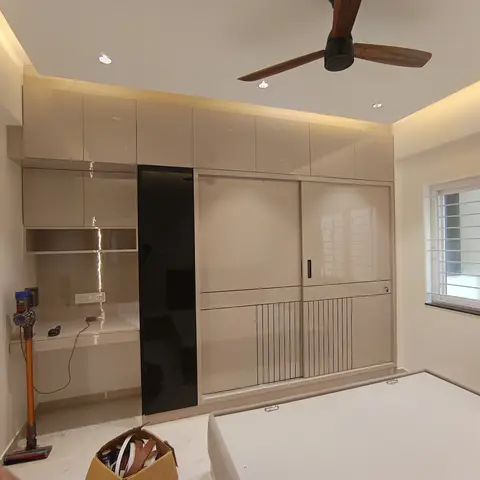 Bedroom with a glossy beige sliding wardrobe accented by a black glass panel, cove-lit ceiling, and a small built-in desk nook