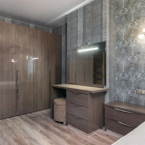 Bedroom with a glossy dark-wood four-door wardrobe, a matching dressing table with a lit mirror