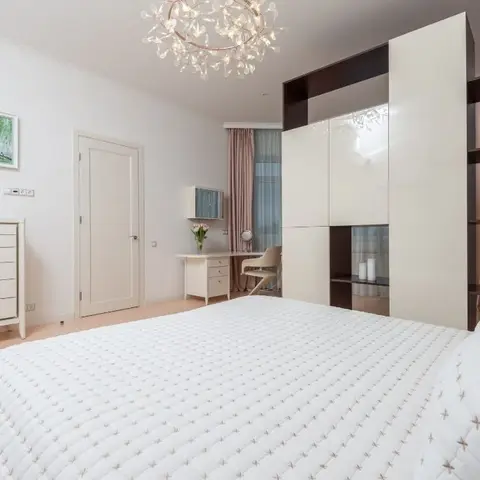 Bedroom with a glossy white and dark-wood wardrobe wall featuring open display niches, a small dressing desk with mirror by the window