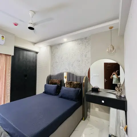 Bedroom with a grey channel-tufted bed edged in gold, navy striped bedding and fur cushions, set against a silver leaf-pattern textured wallpaper panel