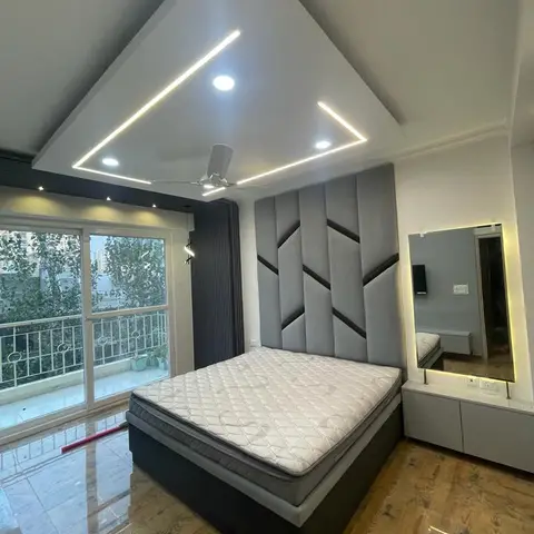 Bedroom with a grey geometric channel-tufted upholstered headboard, a floating dresser with backlit mirror, a box-pattern LED cove ceiling