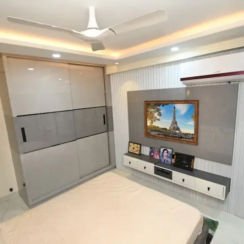 Bedroom with a grey glossy sliding-door wardrobe and a wallpapered TV console wall displaying framed family photographs