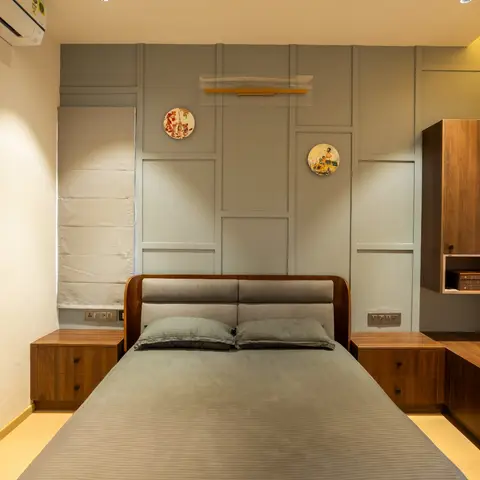 Bedroom with a grey panel-moulding accent wall hung with decorative plates, a curved walnut-and-upholstered headboard bed flanked by matching bedside cabinets
