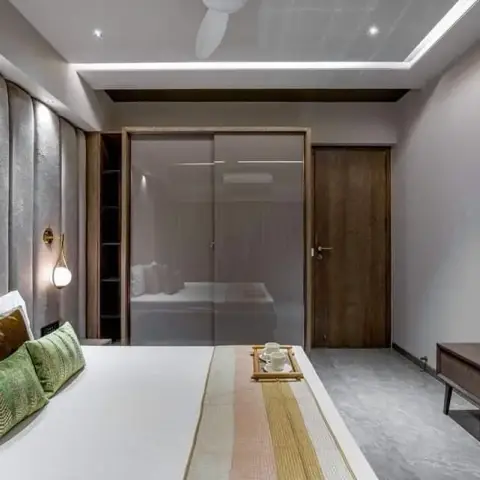 Bedroom with a grey textured panelled wall behind the bed lit by one brass-and-glass sconce, a full-height bronze-mirror sliding wardrobe reflecting the bed