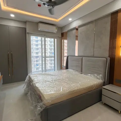 Bedroom with a grey upholstered bed still wrapped in protective plastic, a tall channel-tufted headboard