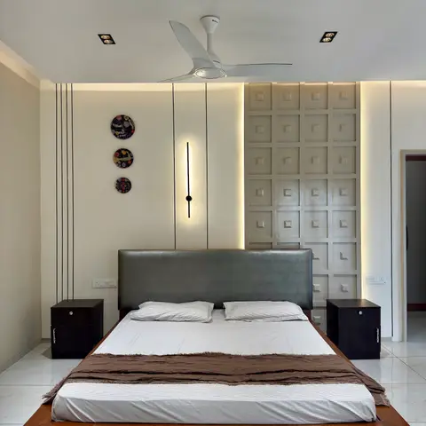 Bedroom with a grey upholstered headboard on a wood platform bed, flanked by matching black nightstands, in front of a backlit 3D coffered feature wall.