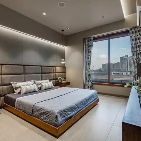 Bedroom with a grid of grey suede upholstered panels forming a full-wall headboard under a lit cove, a low teak platform bed with a wide surround frame
