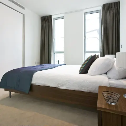 Bedroom with a low walnut platform bed on slim metal legs and a navy quilted throw