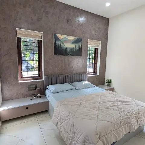 Bedroom with a mauve textured accent wall, a channel-tufted grey upholstered headboard, and floating two-tone nightstands flanking wood-framed windows.