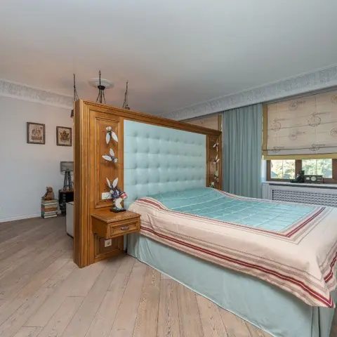 Bedroom with a mint button-tufted headboard set into a tall oak bedback panel with built-in drawer nightstands, wide-plank oak floor