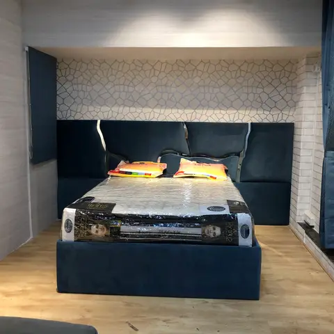Bedroom with a navy channel-tufted upholstered headboard set into a wallpapered niche; mattress still in delivery wrap with tags.