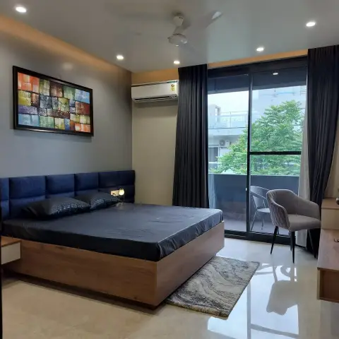 Bedroom with a navy tufted headboard on a wood platform bed, a colourful abstract wall art piece, and a glass door opening to a balcony.
