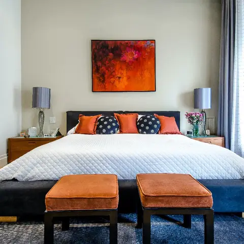 Bedroom with a navy upholstered bed dressed in orange and navy accent pillows, a fiery abstract floral painting above the headboard