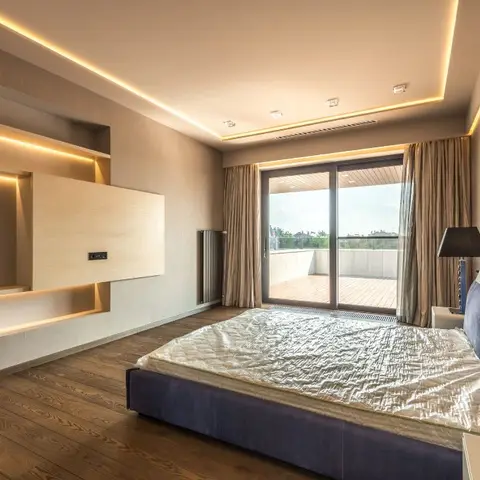 Bedroom with a navy velvet upholstered bed facing a cove-lit shelving wall, damask wallpaper accent, and sliding glass doors opening onto a private terrace.