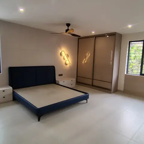 Bedroom with a navy velvet upholstered bed, a bronze mirrored sliding-door wardrobe, and a beige stone-tile accent wall with a sculptural wall sconce.