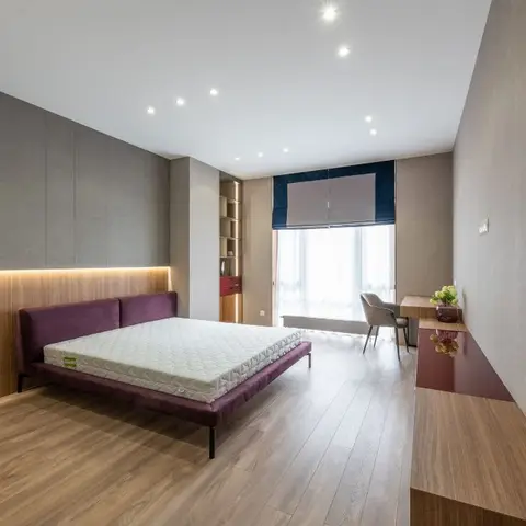 Bedroom with a plum upholstered bed against a grey fabric-panelled wall on a warm-lit wood base, wide-plank wood flooring