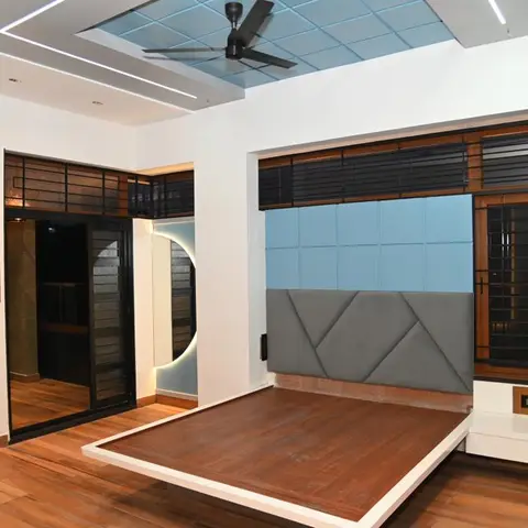 Bedroom with a raised wood platform bed frame, a grey-and-blue geometric quilted headboard wall, and a checkered blue false-ceiling panel above.