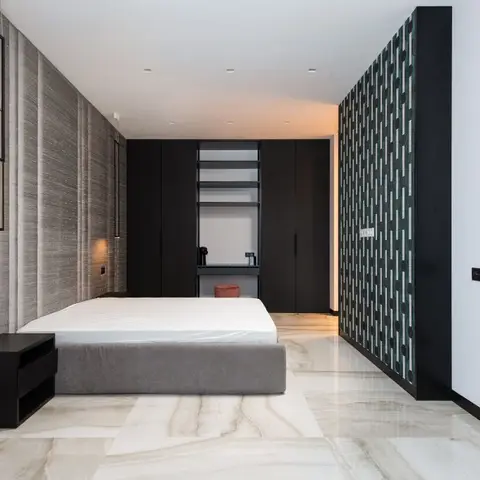 Bedroom with a ribbed grey fabric-panel headboard wall, a matte black wardrobe wall with an open display niche, and a geometric dark accent wall by the door.