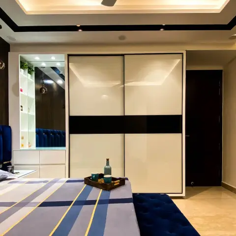Bedroom with a royal-blue velvet channel headboard against dark veneer panelling, a white lacquered-glass sliding wardrobe banded in black