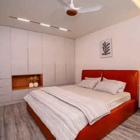 Bedroom with a rust-orange leather upholstered bed facing a full-wall white wardrobe with a backlit display niche and a cove-lit ceiling strip.