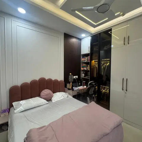 Bedroom with a rust-red scalloped upholstered headboard, pink bedding, and a geometric cove-lit false ceiling beside a glossy wardrobe and open study nook.