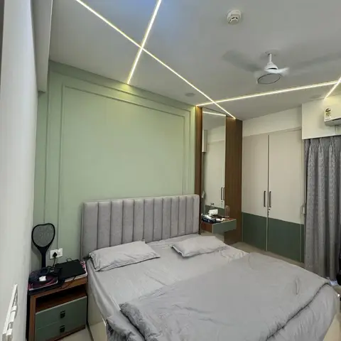 Bedroom with a sage green moulded wall panel behind a channel-tufted grey headboard bed, a criss-cross LED strip false ceiling