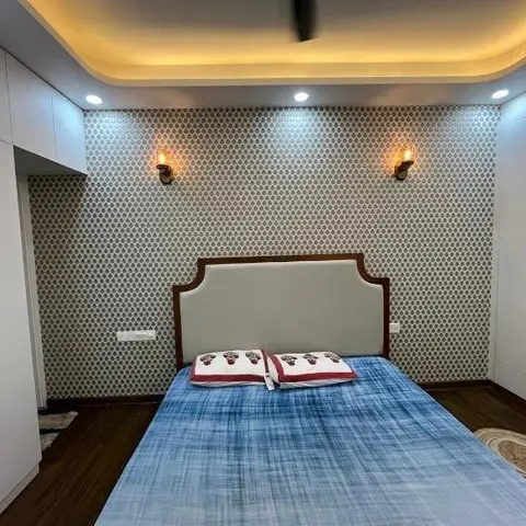 Bedroom with a scallop-patterned wallpaper wall running between two white wardrobe runs, an arched cream upholstered headboard in a wooden frame