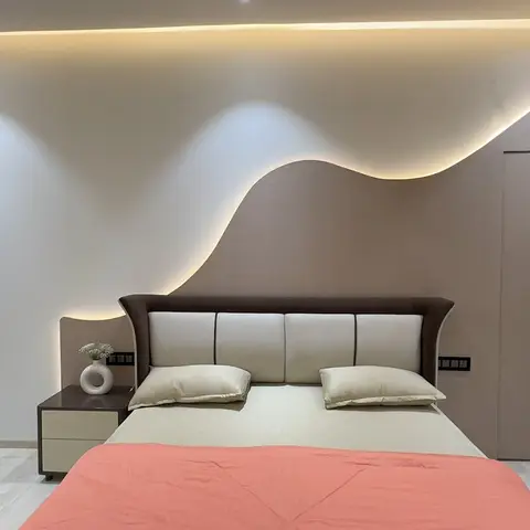 Bedroom with a sculptural wave-shaped cove-lit panel wall rising above an upholstered headboard bed.
