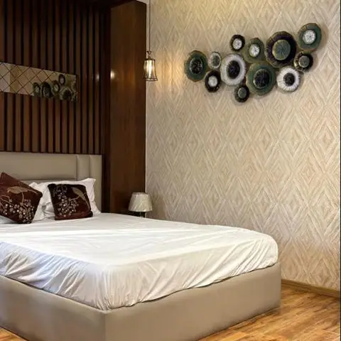 Bedroom with a slatted dark wood plank ceiling detail over the bed and a curated cluster of circular ceramic plates on diamond-pattern textured wallpaper