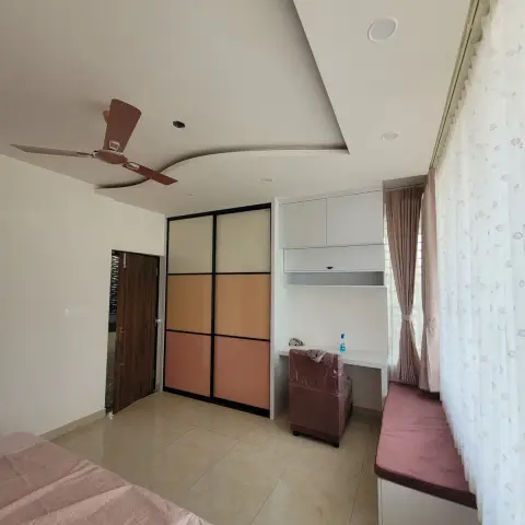 Bedroom with a sliding wardrobe in stacked cream, ochre and salmon glass panels, a white study desk with loft units beside the window and a pink cushioned