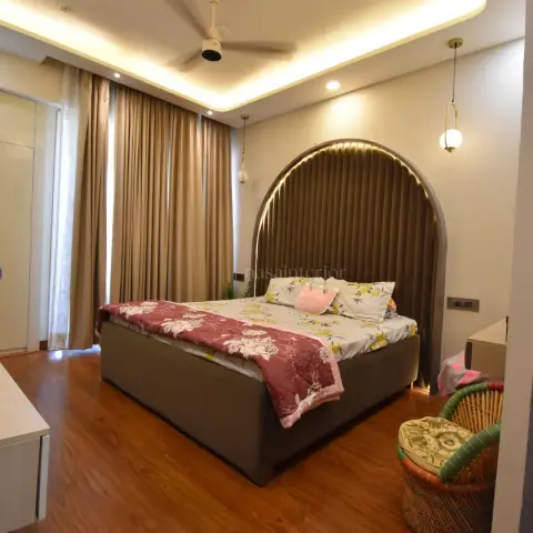 Bedroom with a tall arched fluted headboard in brown suede outlined by a concealed LED strip, two brass-stem globe pendants dropping either side