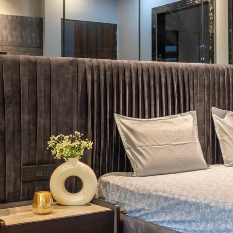 Bedroom with a tall channel-pleated charcoal velvet upholstered headboard and a floating wood nightstand styled with a ceramic vase