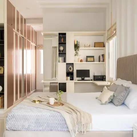 Bedroom with a tall channel-tufted beige headboard beside a built-in white study desk holding a monitor and printer