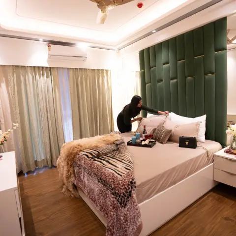 Bedroom with a tall channel-tufted emerald green vertical-panel headboard wall, gold-trimmed mirrored wardrobe, sage curtains and wood flooring
