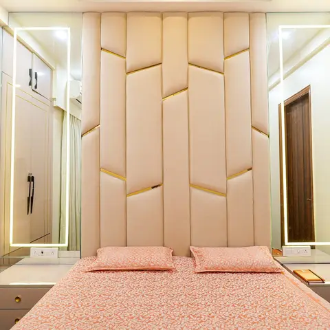 Bedroom with a tall channel-tufted cream headboard trimmed in brass strips, flanked by backlit LED-edge mirrors over matching gold-handled bedside units.