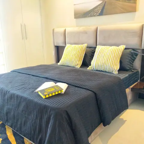 Bedroom with a tall channel-tufted grey velvet headboard, charcoal striped bedding with mustard-striped cushions