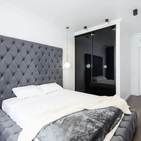 Bedroom with a tall diamond-tufted grey velvet headboard, a black mirrored sliding wardrobe, and matching pendant lights flanking the bed.