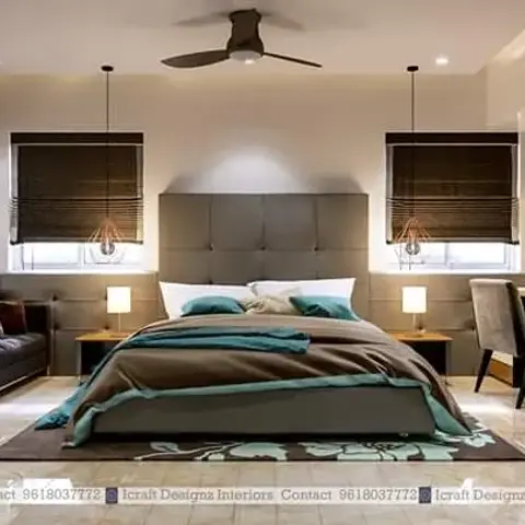 Bedroom with a tall grey channel-tufted headboard, teal-and-brown bedding, twin pendant bedside lights, and a dark tufted bench sofa at the foot of the bed.